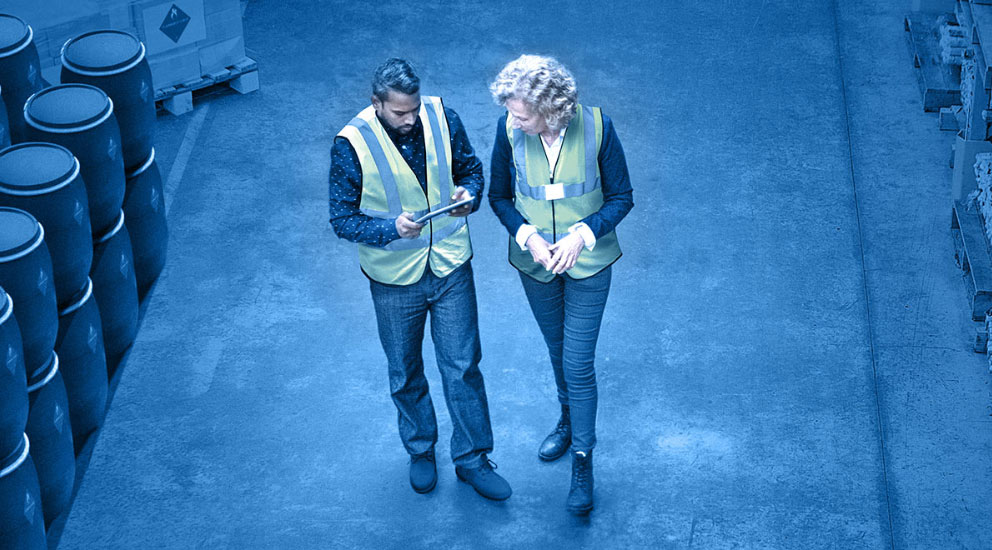 Interior of warehouse with two staff walking and reviewing warehouse management system