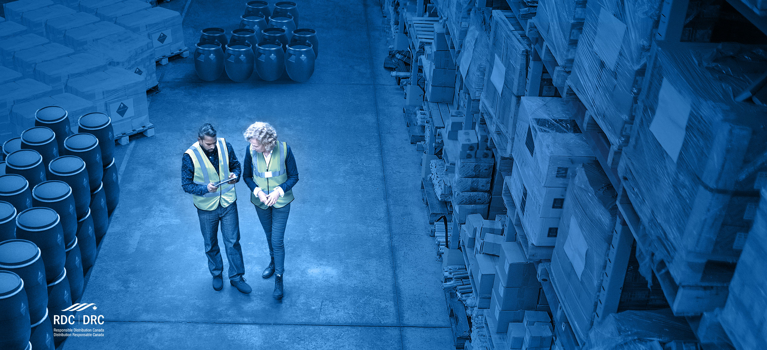 Interior of warehouse with two staff walking and reviewing warehouse management system